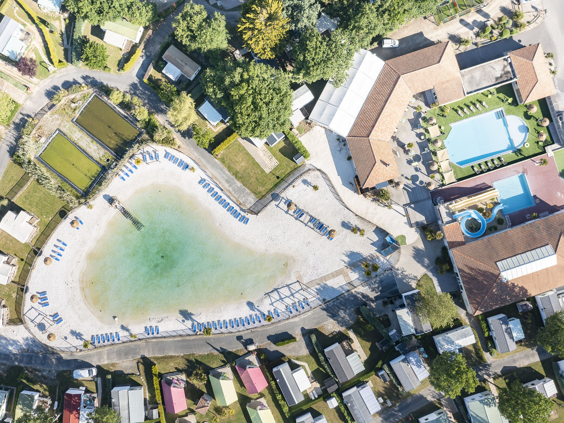 Vue aérienne village vacances avec piscine et plage.
