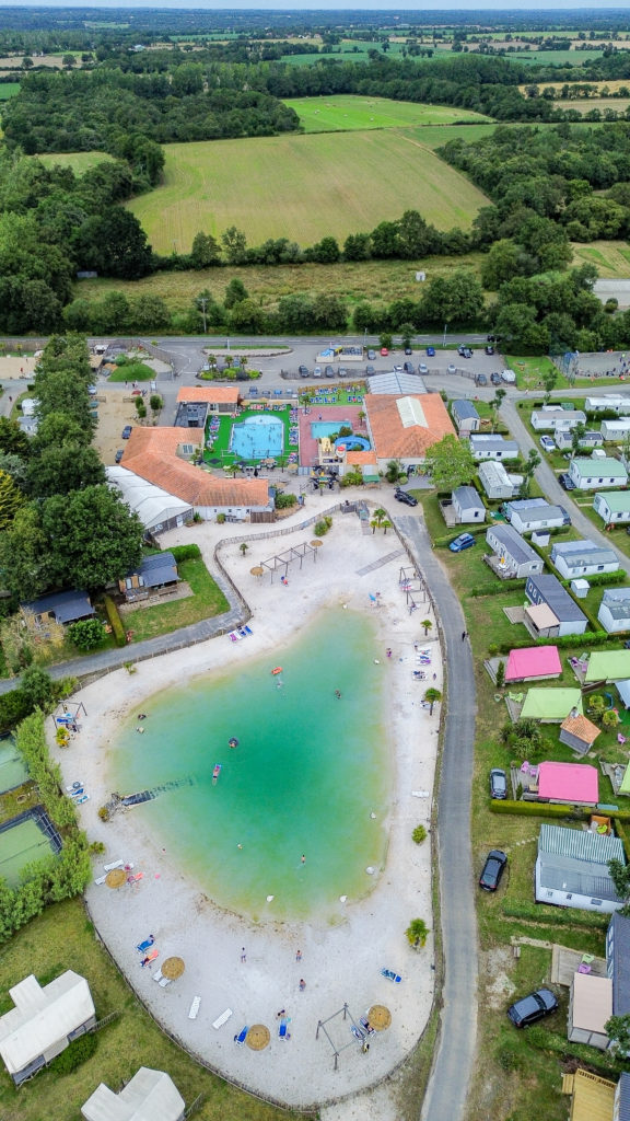 Vue aérienne camping avec piscine et plage artificielle.